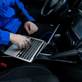 Technician using laptop inside car for diagnostics.